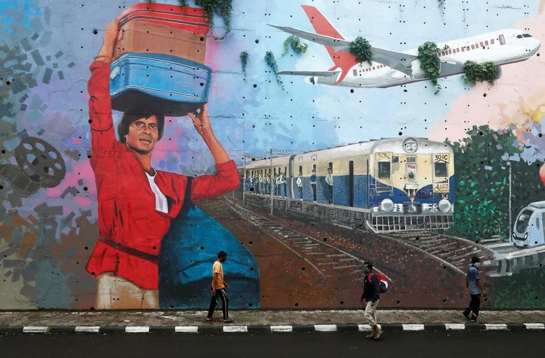 People wearing protective masks walk past a mural of Bollywood actor Amitabh Bachchan, after he and other members of his family tested positive for the coronavirus disease (COVID-19) in Mumbai. REUTERS/Francis Mascarenhas